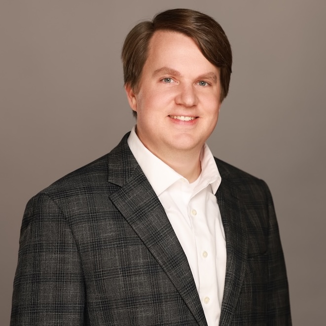 A photo of Cody wearing a gray and white plaid shirt standing against a gray background